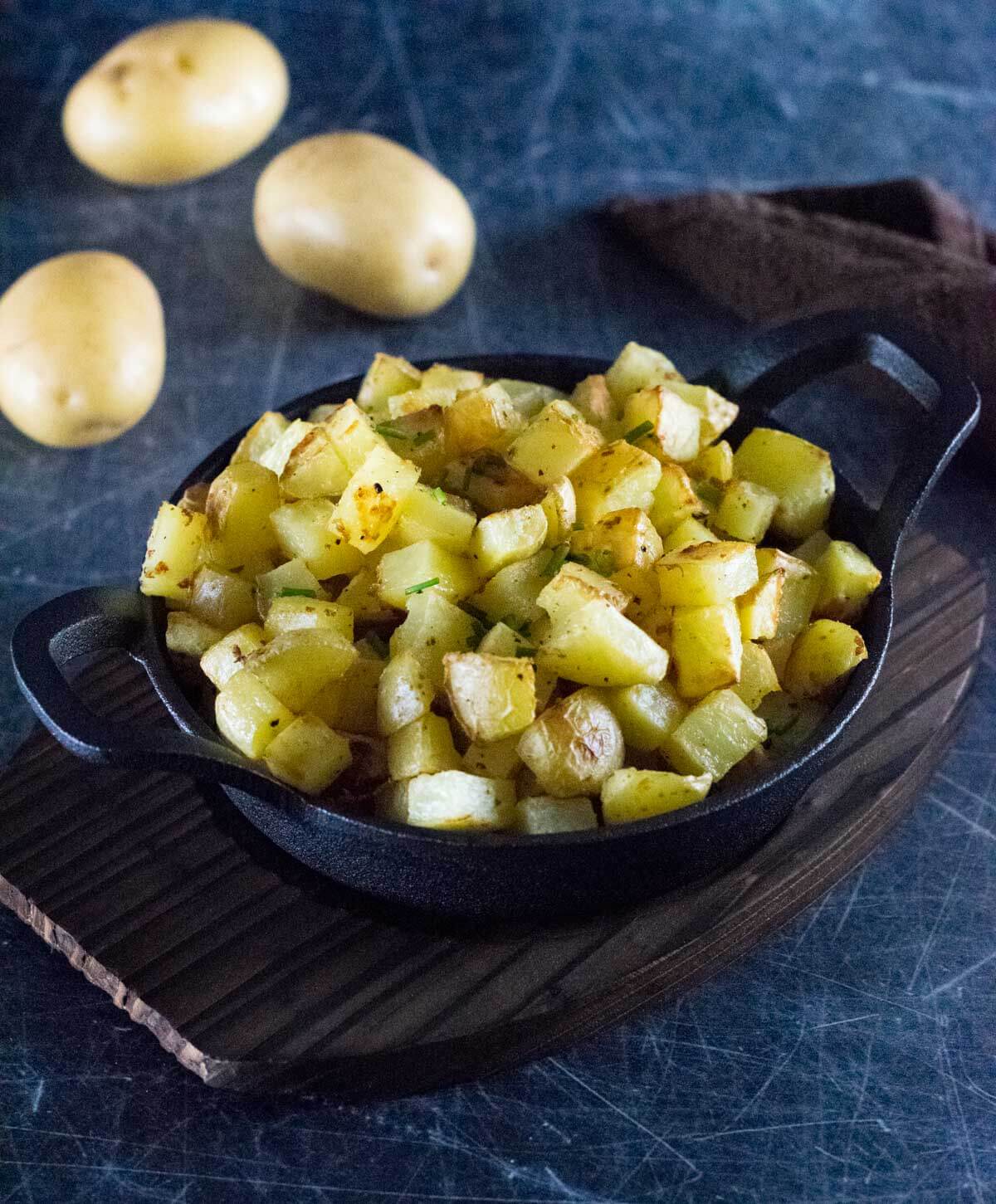 Breakfast potatoes in cast iron dish with raw potatoes sitting behind.