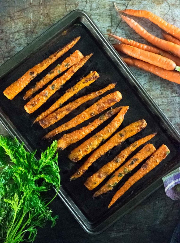 Parmesan Roasted Carrots on brown pan with raw carrots alongside.