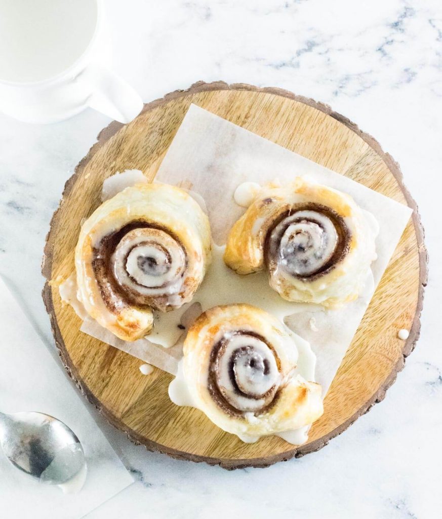 Puff pastry cinnamon rolls on tray drizzled with icing.