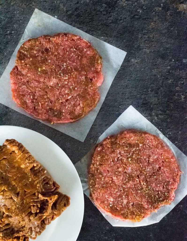 Raw chorizo burger patties on wax paper with raw chorizo on white plate.