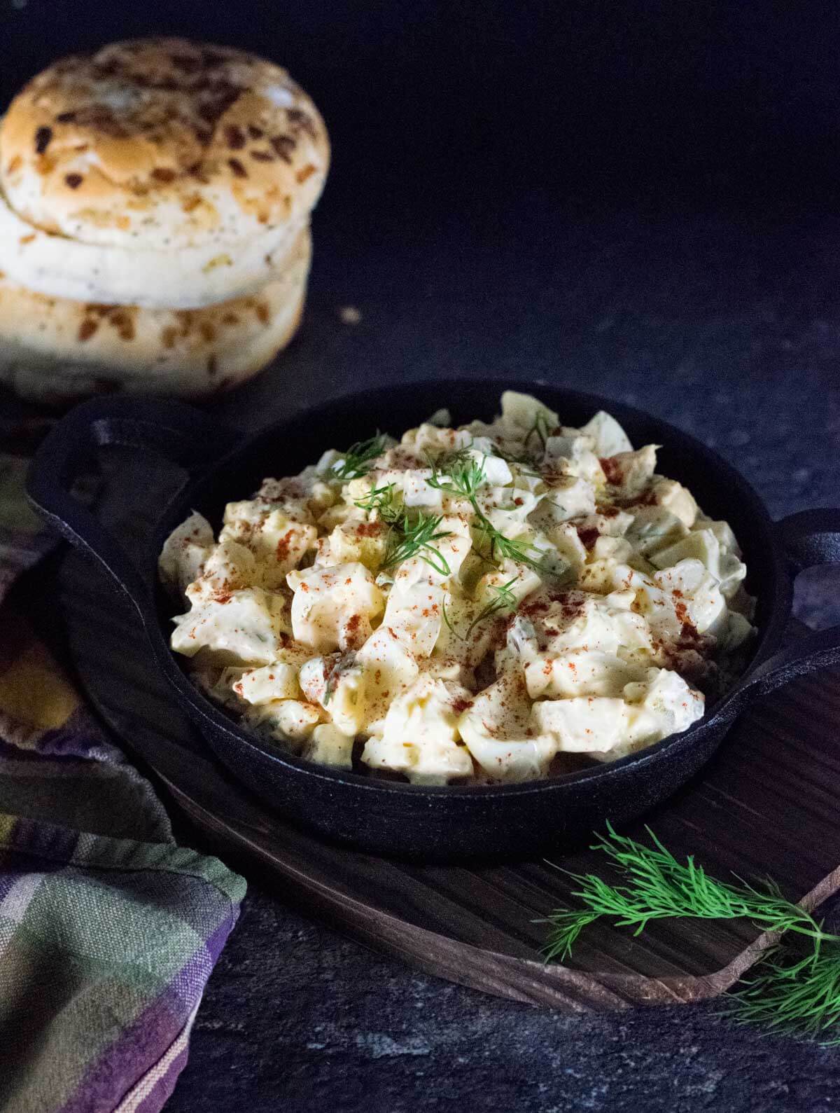 Egg Salad in serving dish with onion rolls behind.