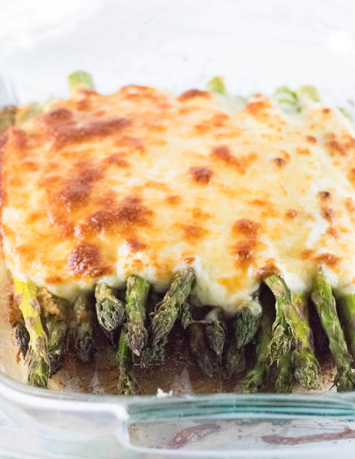 Close up view of baked asparagus with cheese melted on top.