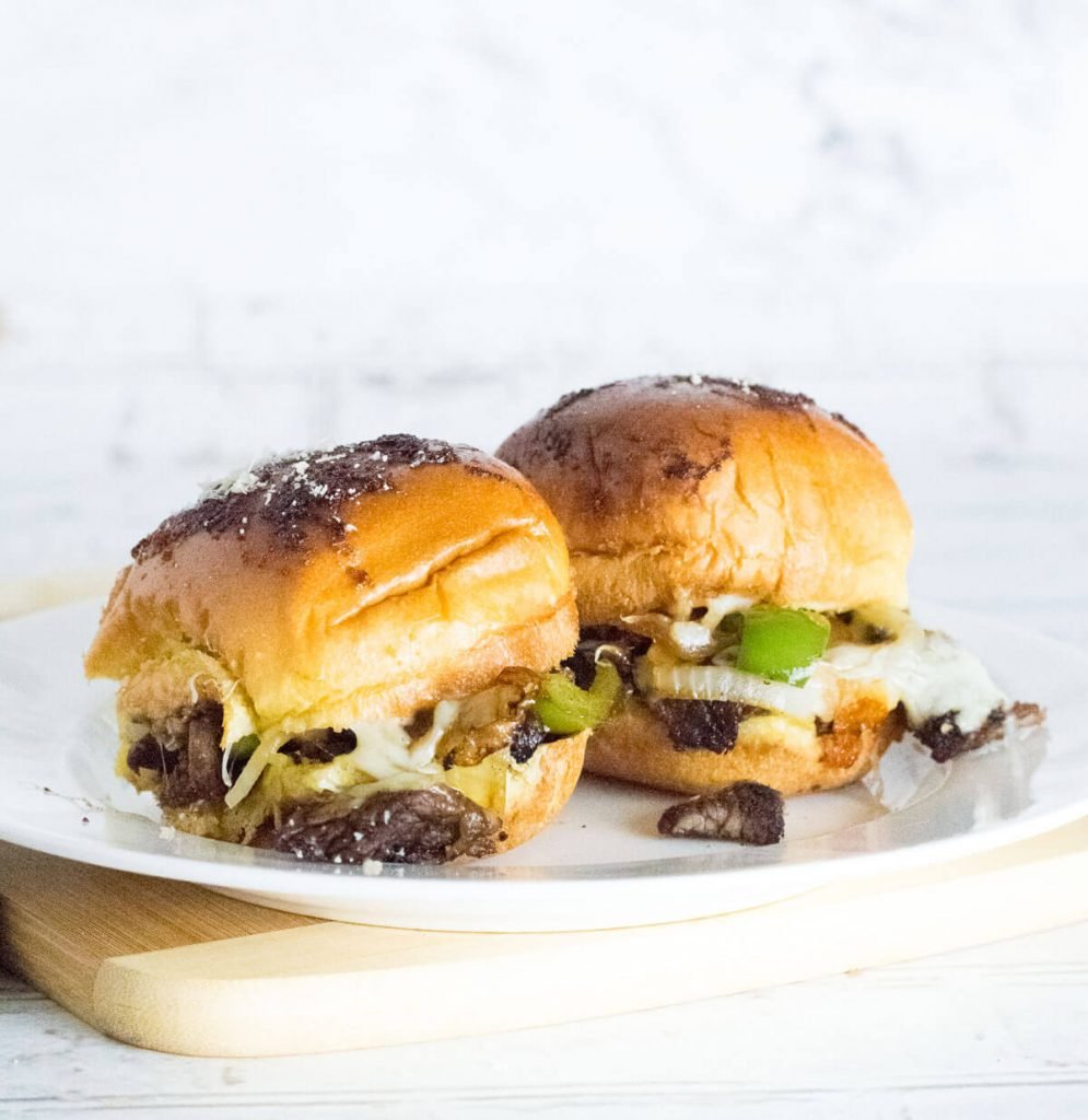 Two Philly cheesesteak sliders on a white plate.