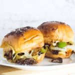 Two Philly cheesesteak sliders on a white plate.