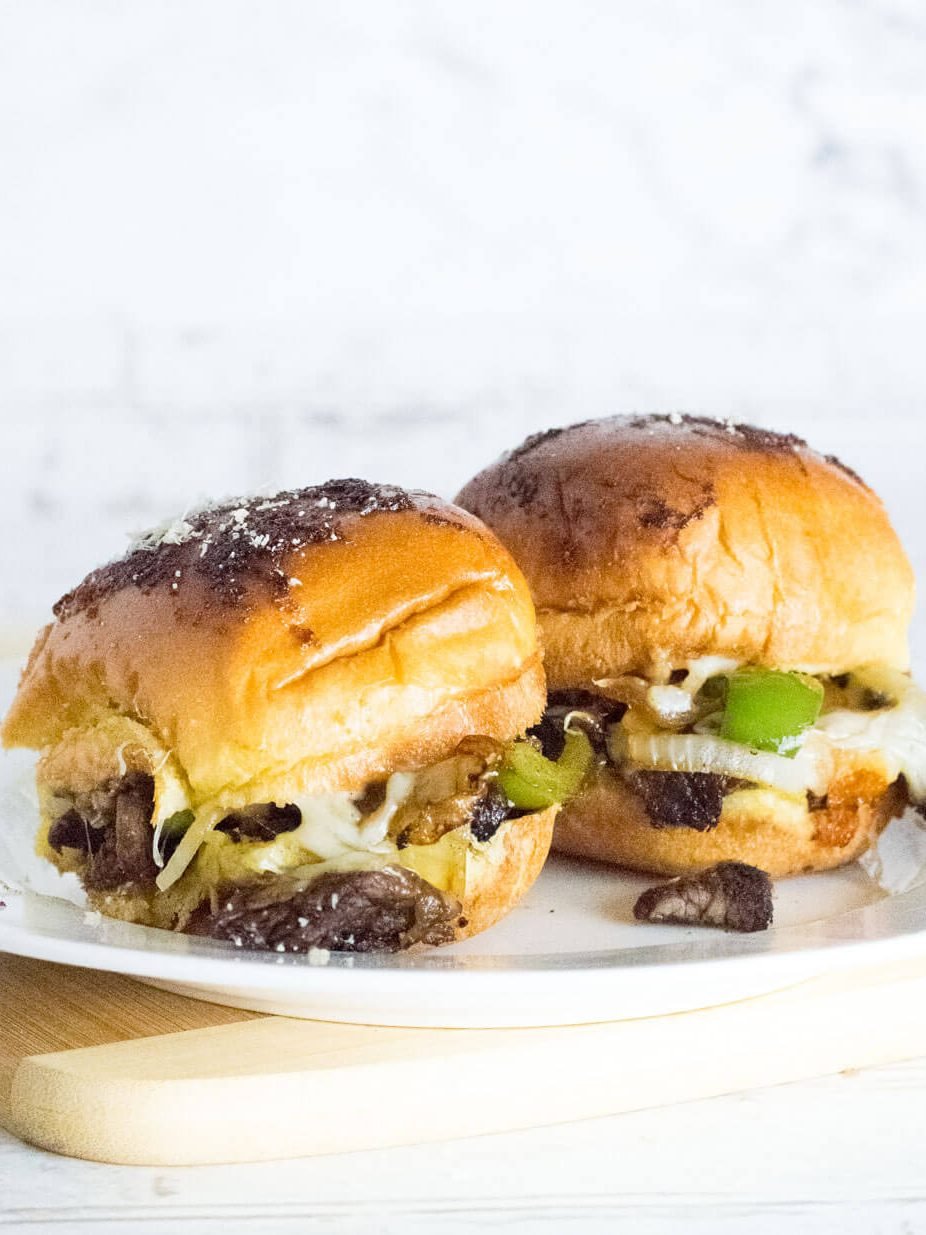Two Philly cheesesteak sliders on a white plate.