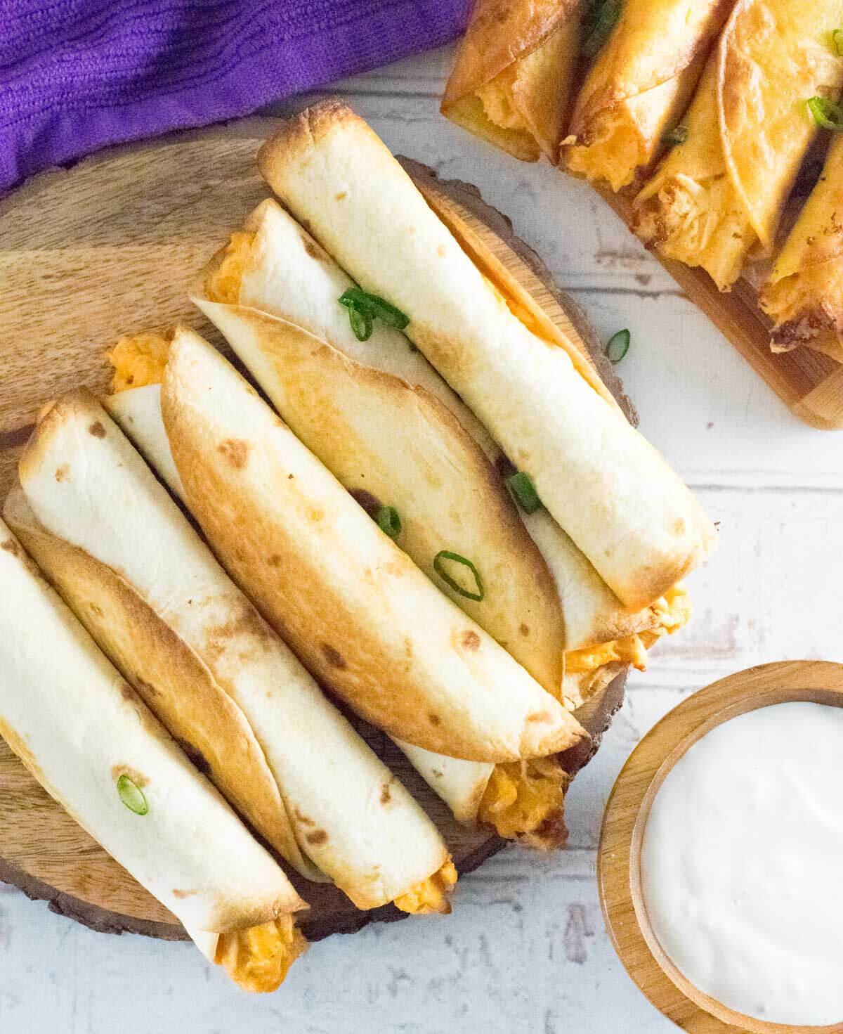 Baked buffalo chicken taquitos on wooden tray shown from above.