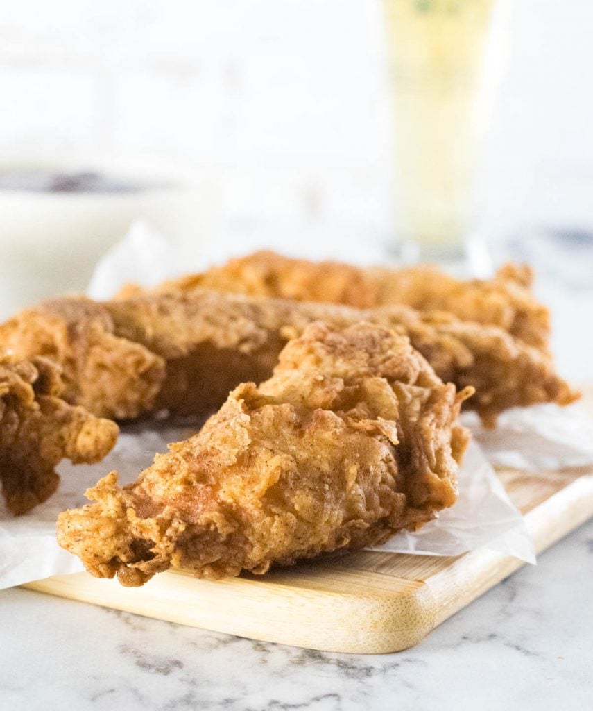 Beer battered chicken tenders on small cutting board.