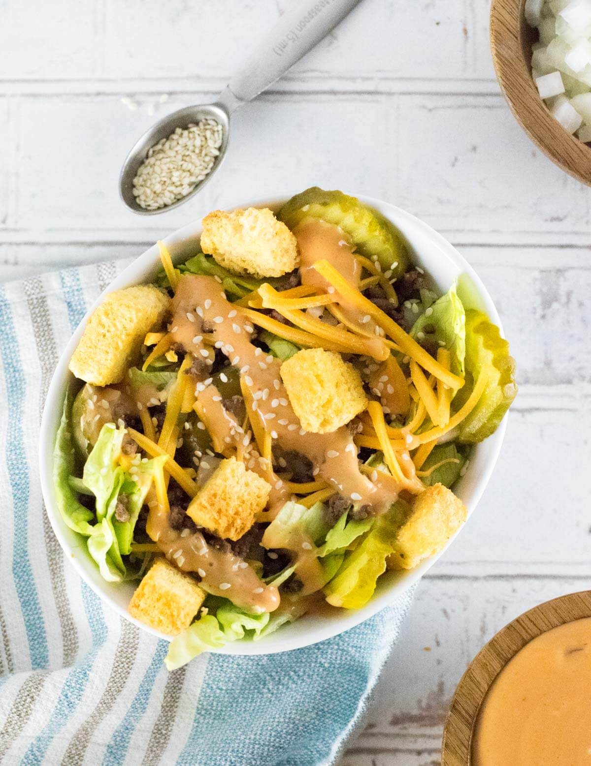 Big Mac Salad with Big Mac Sauce next to it and spoon full of sesame seeds.