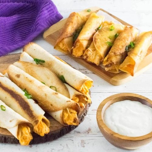 Buffalo chicken taquitos served with dipping sauce on wooden trays.