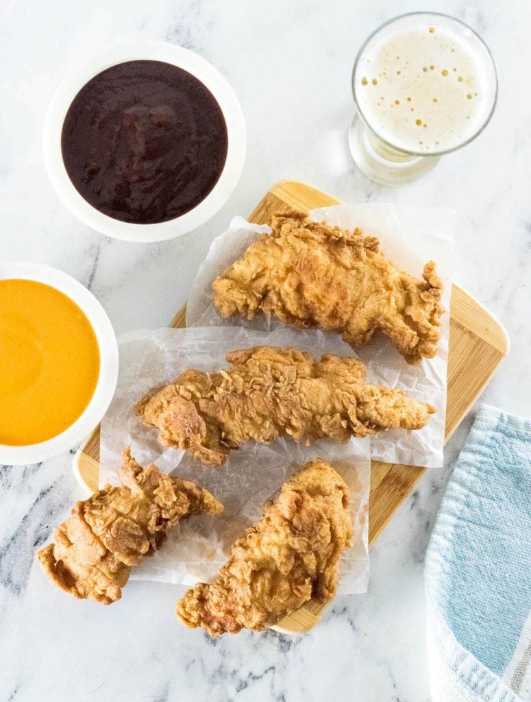 Crispy chicken tenders on wax paper with dipping sauces.