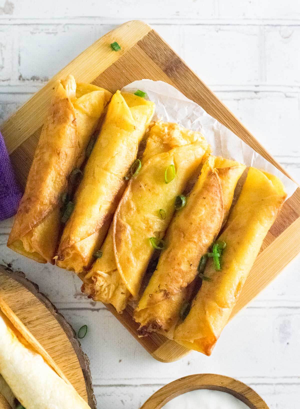 Fried buffalo chicken taquitos on cutting board.