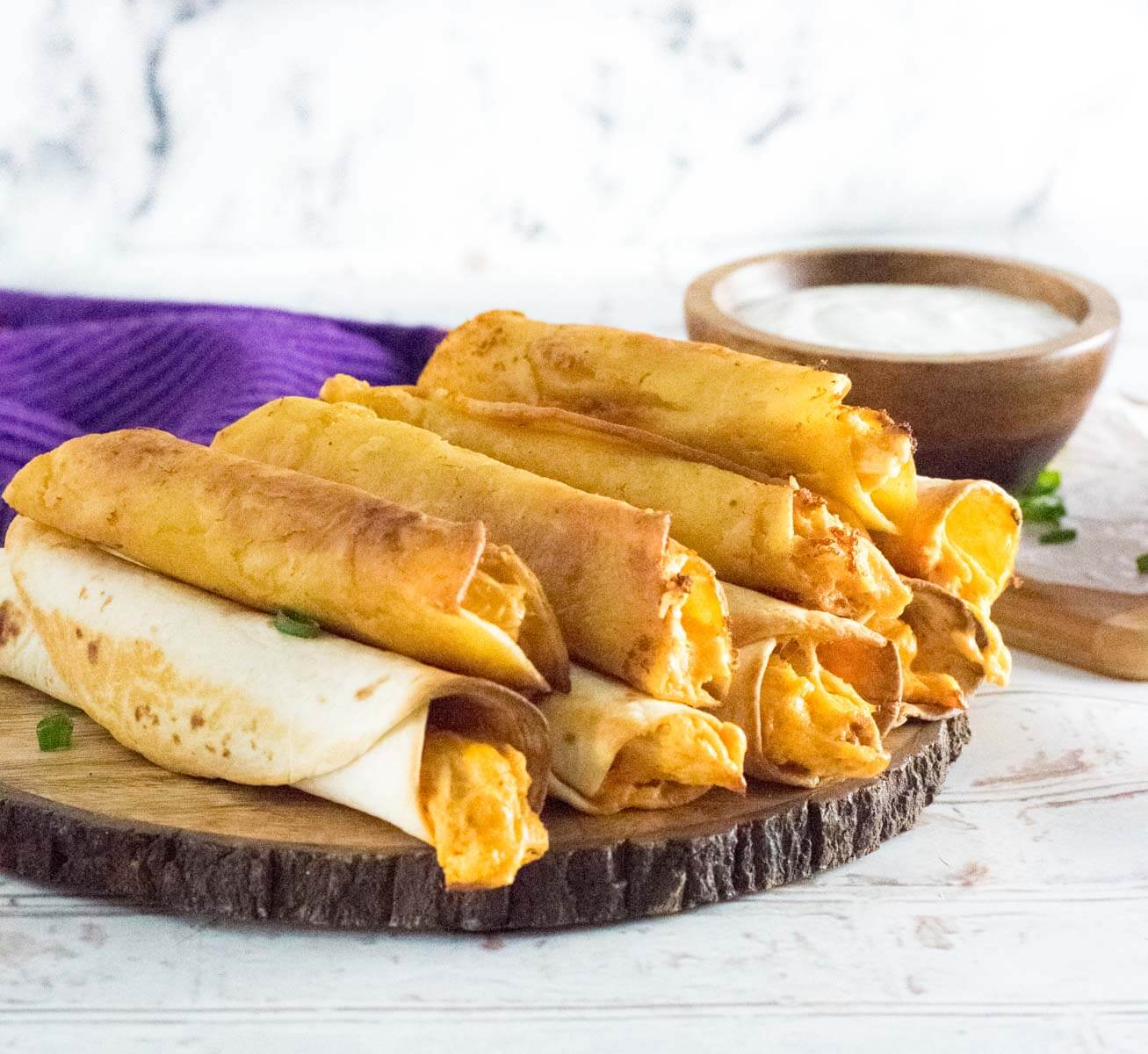 Baked and fried taquitos served with dipping sauce with a purple towel shown. 
