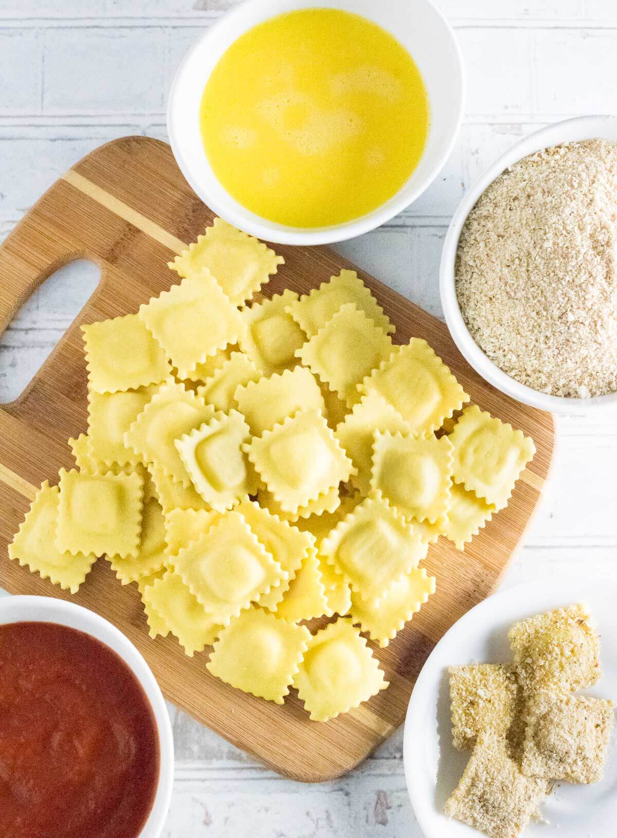 Toasted ravioli ingredients, showing egg wash, breadcrumbs, ravioli and marinara.