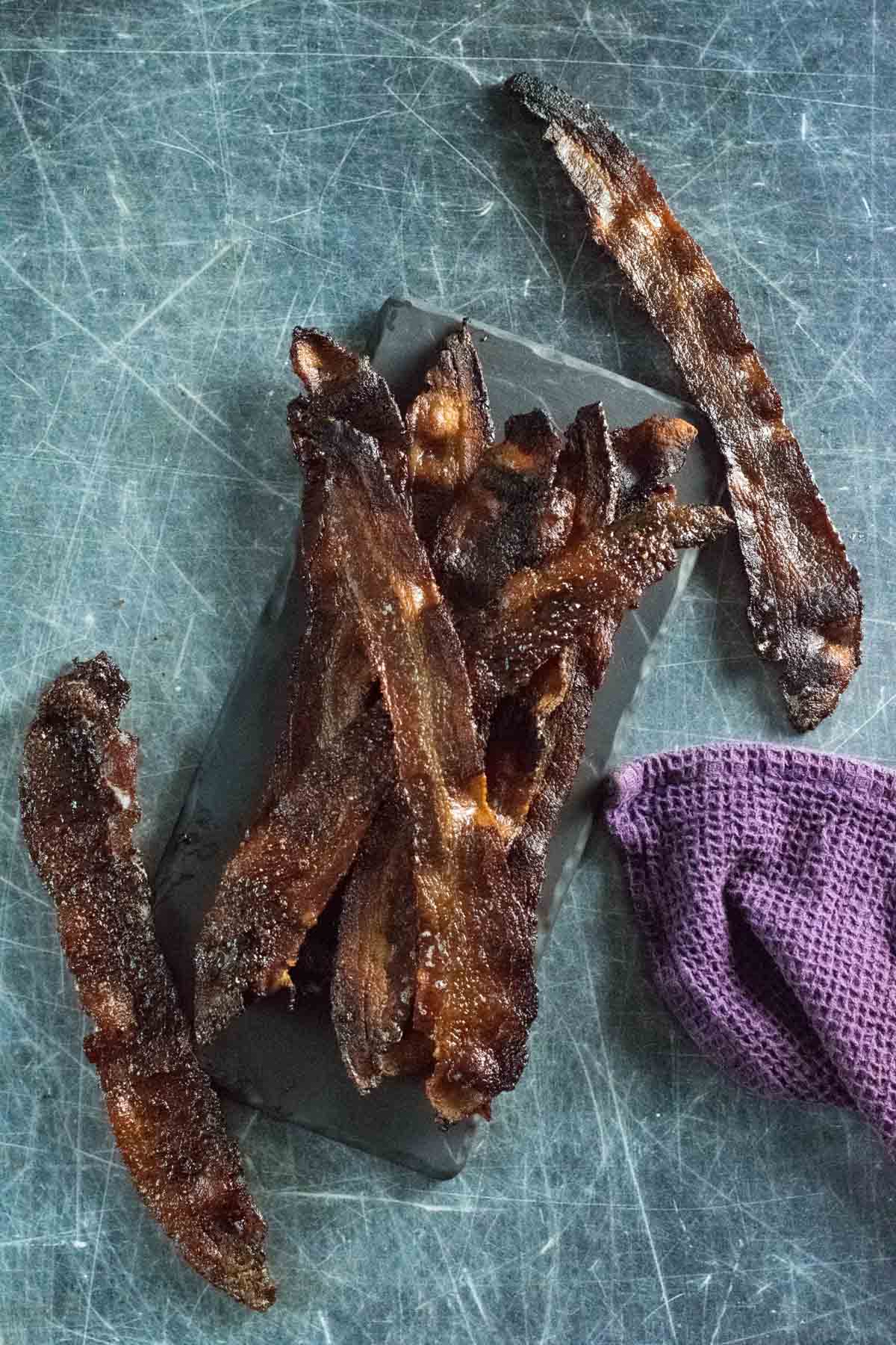 Candied bacon on black tray.