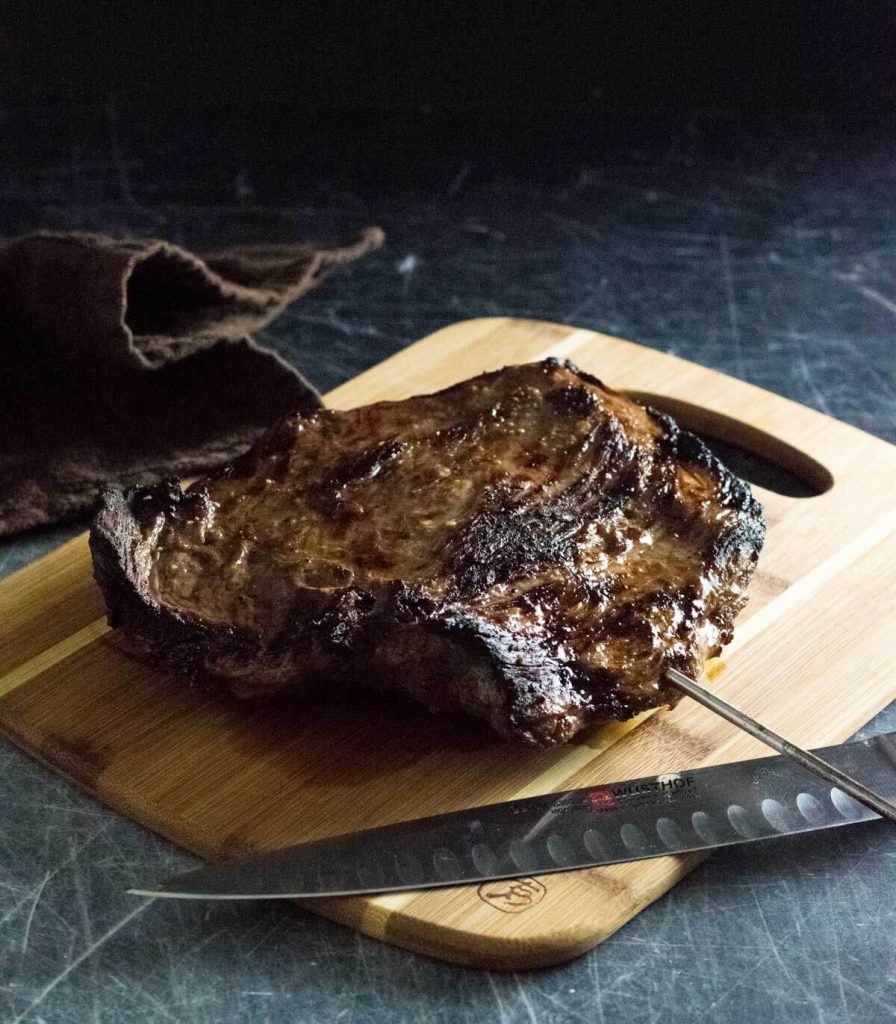 Broiled flank steak resting on cutting board with sharp knife.