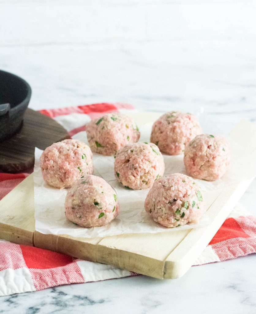 Raw meatballs on parchment paper in a single layer.