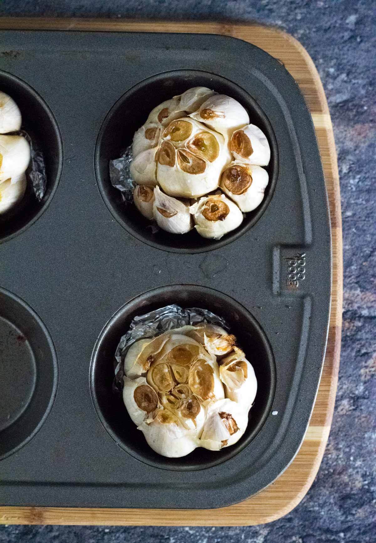 Roasted heads of garlic in a muffin tin.