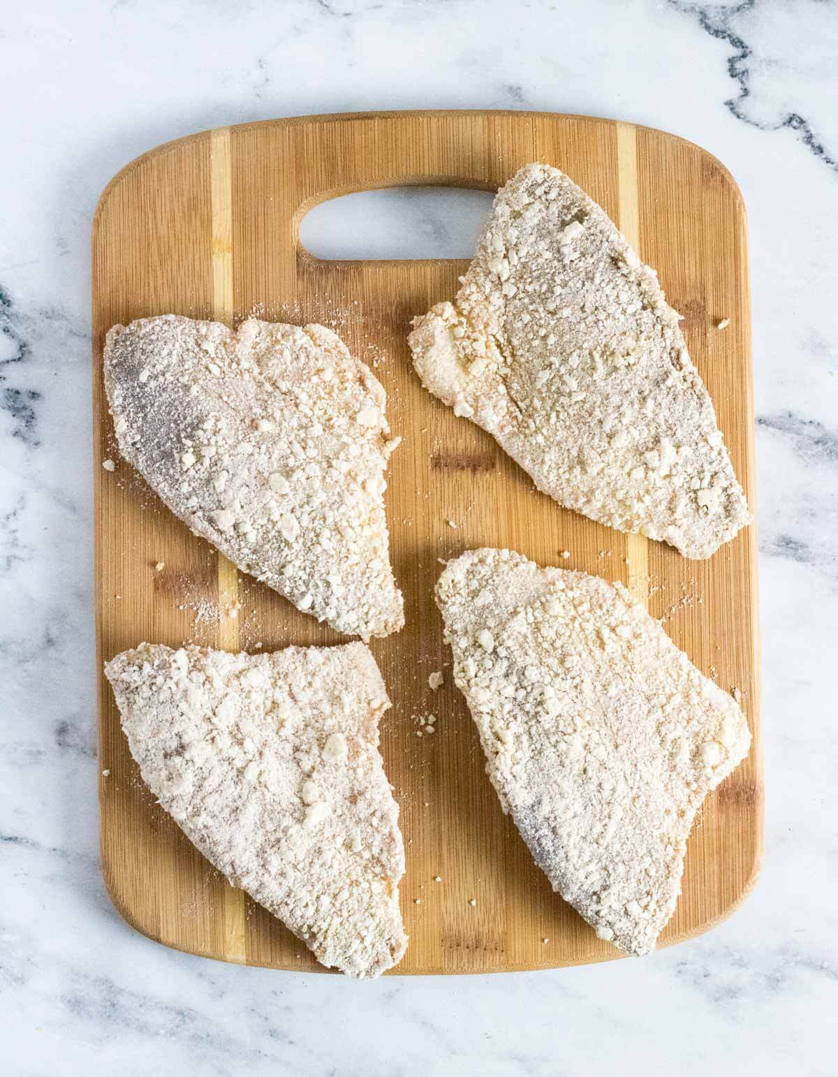 Breaded raw perch fillets on cutting board.