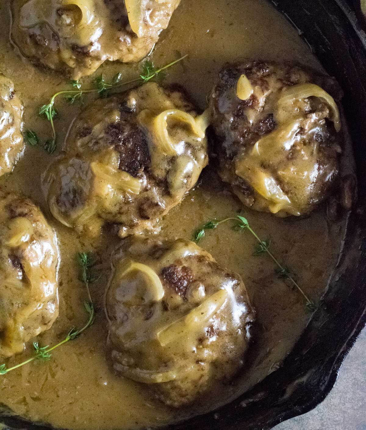 Cooking Salisbury steaks, simmering in onion gravy.